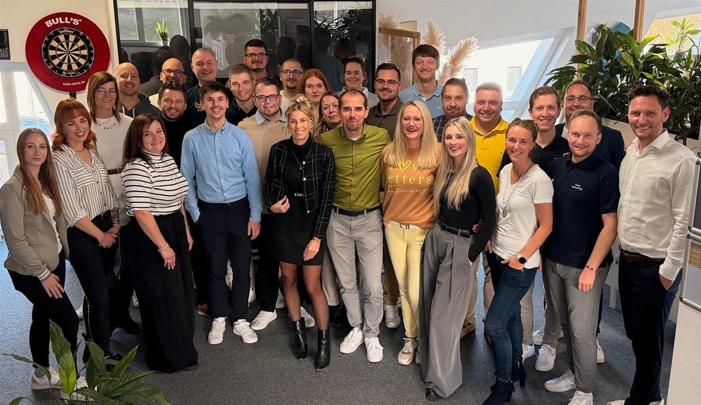 Rund 30 Mitarbeiterinnen und Mitarbeiter des Teams Falk Stiefler stehen lachend zusammen im Büro in Klipphausen.